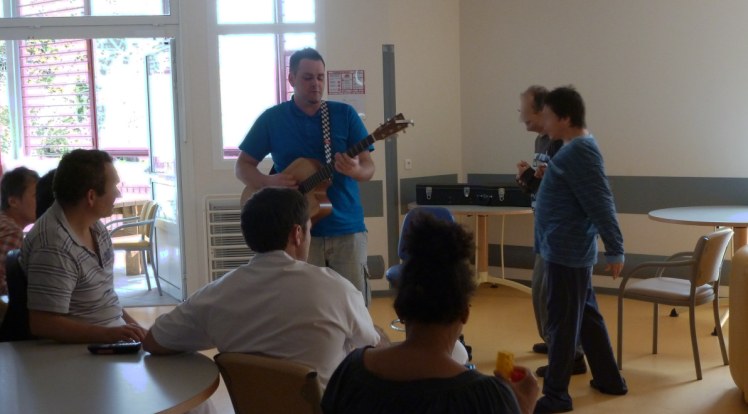 Raphaël Hiraboure jouant de la guitare et chantant au sein d'un pavillon de l'hôpital marin en présence de patients assis et debout