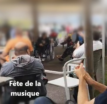 Au premier plan des mains qui applaudissent, puis un patient à la percussion et divers patients en fauteuil roulant qui assistent à la fete