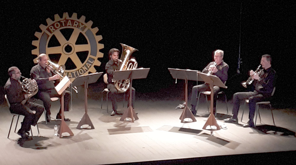 5 instrumentistes (à vent) sur scène et logo du Rotary