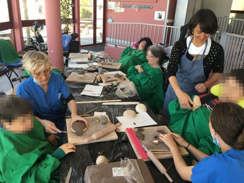 4 patients vêtus de blouses vertes autour de la table d'atelier céramique avec 3 personnes : animatrice et agents de l'hôpital marin
