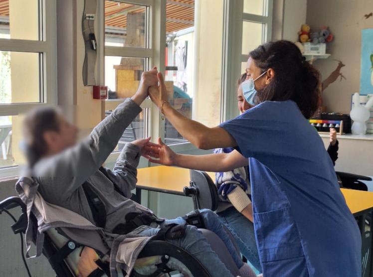 une patiente sur fauteuil roulant tend la main vers la danseuse qui la saisit et danse avec elle