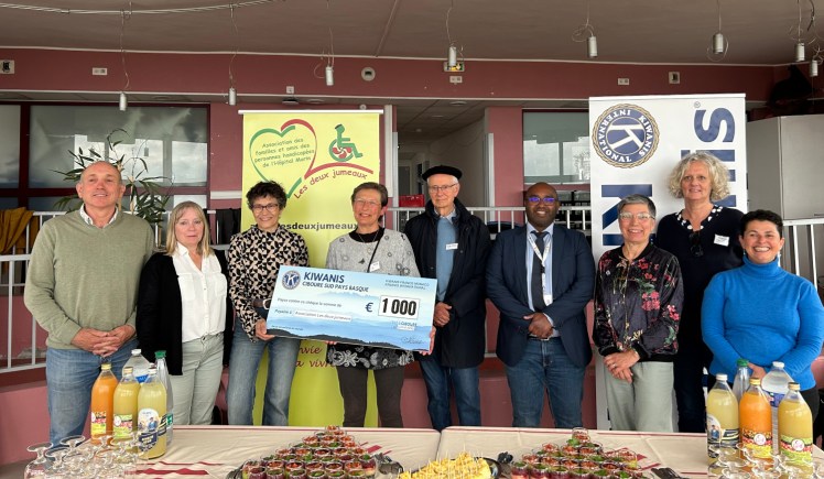 un groupe de 9 personnes des Kiwanis de Ciboure, de l'association et de l'Hôpital Marin de Hendaye, dont 2 personnes tiennent un grand chèque de 1000€. Deux monolés derrière de l'association les deux jumeaux et des kiwanis, au premier plan le buffet préparé par l'hôpital marin