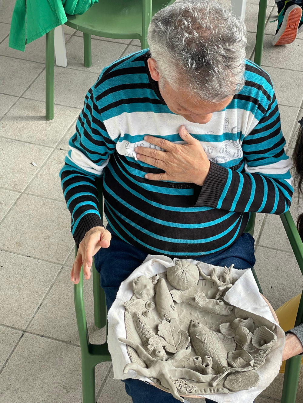 un patient assis regardant sur ses genoux une assiette palissy de glaise non cuite